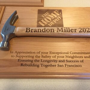May include: A wooden plaque with a hammer on top. The plaque is engraved with the text "The Home Depot", "Brandon Miller 2023", and "In Appreciation of your Exceptional Commitment to Supporting the Safety of your Neighbors and Ensuring the Longevity and Success of Rebuilding Together San Francisco".