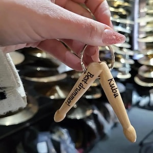 May include: A pair of wooden drumsticks with a keychain ring. One drumstick is engraved with "Best Drummer!" and the other is engraved with "Kuba".