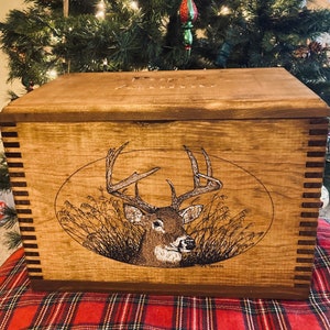 May include: A wooden box with a deer design engraved on the front. The box has a hinged lid and is made of natural wood. The deer is a white-tailed buck with large antlers. The box is a great way to store and display hunting or fishing gear.