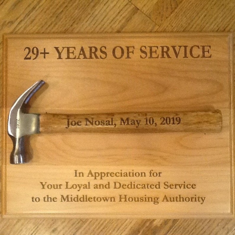 May include: A wooden plaque with the text "29+ YEARS OF SERVICE" and "Joe Nosal, May 10, 2019". Below the text is a hammer with a wooden handle. The plaque also includes the text "In Appreciation for Your Loyal and Dedicated Service to the Middletown Housing Authority."