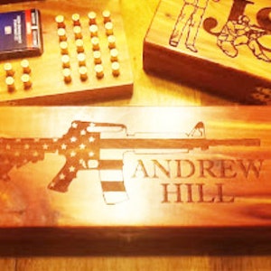 May include: A wooden box with an engraved image of an assault rifle with an American flag design. The box is personalized with the name "ANDREW HILL".