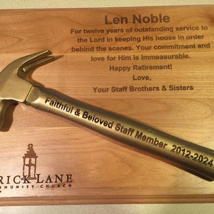 May include: A wooden plaque with a gold-colored hammer on top. The plaque has an inscription that reads "Len Noble For twelve years of outstanding service to the Lord in keeping His house in order behind the scenes. Your commitment and love for Him is immeasurable. Happy Retirement! Love, Your Staff Brothers & Sisters Faithful & Beloved Staff Member 2012-2024 Brick Lane Community Church".