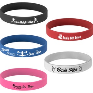 May include: Five different silicone wristbands with various colors and text. The wristbands are black, red, blue, gray, and pink. The text on the wristbands reads "Sun Heights Run", "Sam's Gift Drive", "Fighting Knights Cheer Team", "Bride Tribe", and "Racing for Hope".