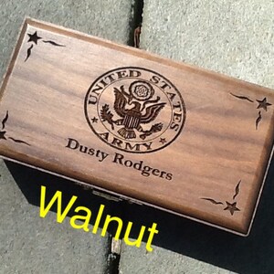 May include: A wooden box with a dark walnut finish. The box has an engraved United States Army seal with the words 'United States Army' and a star. The box also has the words 'Dusty Rodgers' engraved on it. The box has a star design on each corner.