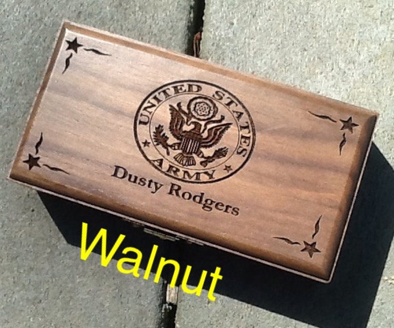 May include: A wooden box with a dark walnut finish. The box has an engraved United States Army seal with the words 'United States Army' and a star. The box also has the words 'Dusty Rodgers' engraved on it. The box has a star design on each corner.