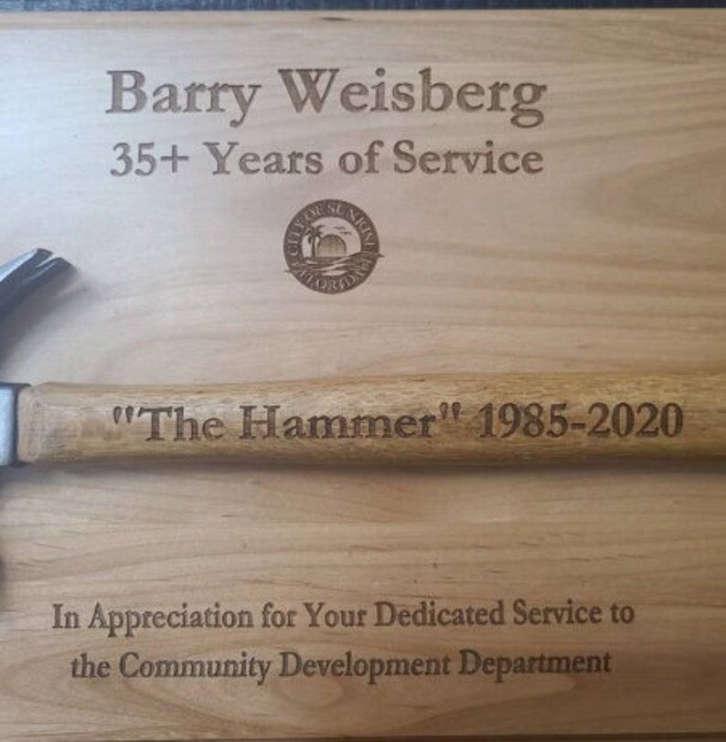 May include: A wooden plaque with the text "Barry Weisberg 35+ Years of Service" and a city seal. The plaque also has the text "The Hammer" 1985-2020 and "In Appreciation for Your Dedicated Service to the Community Development Department".
