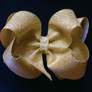 May include: A large gold glitter bow with a center loop. The bow is made of a soft, shimmery fabric.