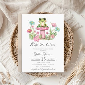 Puede incluir: Una invitación para baby shower con una ilustración en acuarela de una rana verde sentada en una seta rosa rodeada de flores coloridas. El texto "hop on over" se muestra junto con los detalles del baby shower de Bella Rowan, incluyendo fecha, hora y lugar.