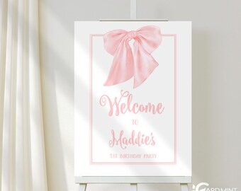 May include: A pink welcome sign with a large pink bow on top. The sign says "Welcome to Maddie's 1st Birthday Party".