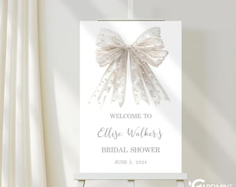 May include: A white bridal shower welcome sign featuring a large white bow with pearl accents. The sign reads "Welcome to Elise Walker's Bridal Shower June 2, 2024".