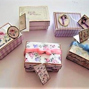 May include: Five small decorative boxes with various floral and patterned designs. The boxes are stacked in pairs and feature ribbon accents and small tags.