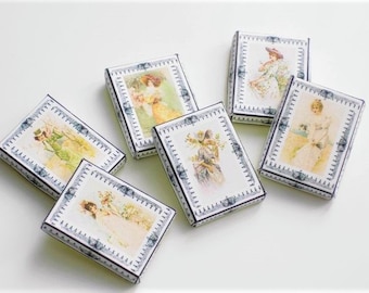 May include: Six small boxes with blue and white trim, each featuring a different vintage illustration of a woman in a dress. The boxes are arranged in a semi-circle on a white surface.