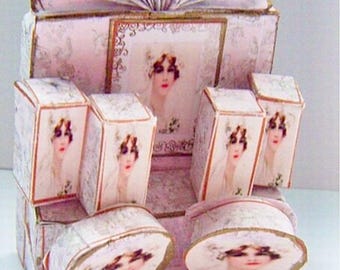 May include: A decorative, multi-tiered display piece in shades of pink and gold. The piece features a fan-shaped top, a central framed image, and several smaller boxes and hat-shaped elements, all adorned with vintage portraits.