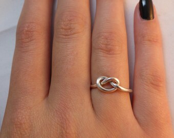 Op de afbeelding: Een zilveren knoop ring op een hand met zwarte nagellak.
