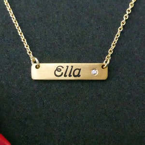 May include: Gold necklace with a bar pendant that says "Ella" and a small diamond accent.