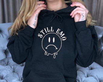 May include: Black hooded sweatshirt with a white graphic of a dripping sad face and the text "STILL EMO".