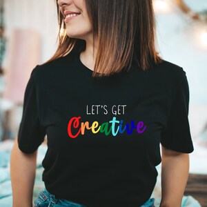 May include: A black t-shirt with the text "Let's Get Creative" in rainbow colors.