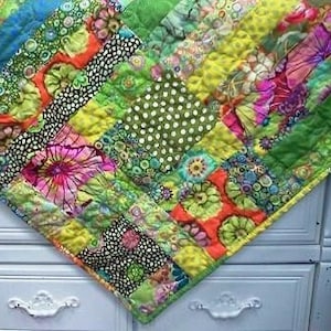 May include: A colourful patchwork quilt featuring a variety of floral patterns in shades of green, yellow, pink, and orange. The quilt is made from different fabrics and textures, creating a unique and eye-catching design.