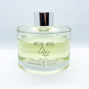 May include: A clear glass bottle with a silver lid filled with a light yellow liquid. The label reads "WITCHIE WICKS" with a triangle logo and the text "Made in D.C. Oil Based & Alcohol Free | Duration 6+ Months Himalayan Bamboo 6.5 fl oz".