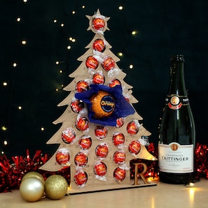 May include: A wooden Christmas tree advent calendar with 24 numbered doors, filled with red and orange chocolate truffles. A bottle of Taittinger Champagne is in the foreground, with red and gold tinsel.