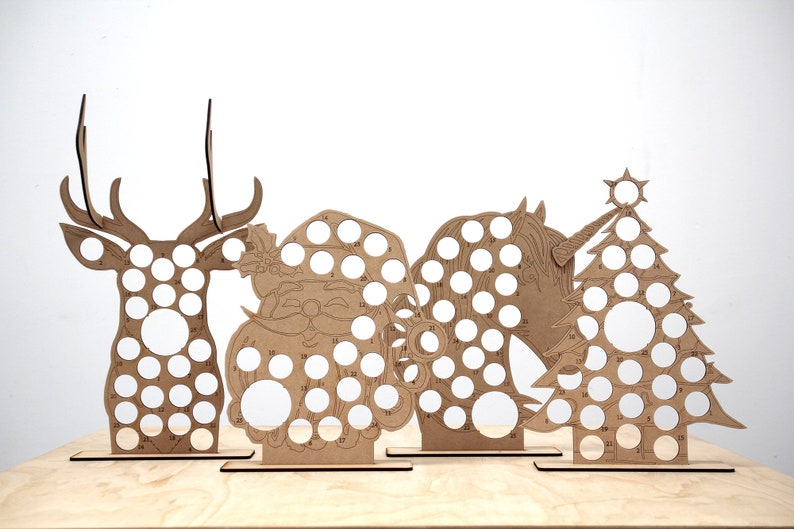 May include: Four wooden Christmas countdown advent calendars, each featuring a different design: a reindeer, Santa Claus, a unicorn, and a Christmas tree. Each design has 24 numbered circles for placing treats or small gifts.