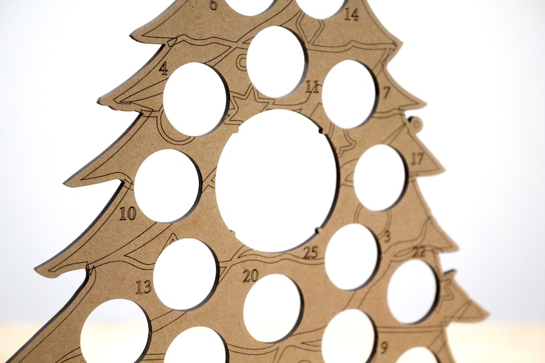 May include: A brown wooden Christmas tree ornament holder with 25 numbered circles for holding ornaments. The tree is made of plywood and has a rustic look.