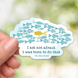 May include: A sticker with a blue and yellow fish design. The sticker has a quote that reads 'I am not afraid. I was born to do this. -St. Joan of Arc.'