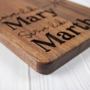 May include: A wooden cutting board with the names "Love Like Mary" and "Serve Like Martha" engraved on it.