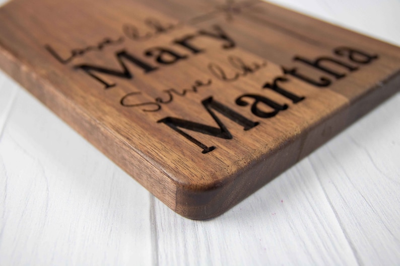 May include: A wooden cutting board with the names "Love Like Mary" and "Serve Like Martha" engraved on it.