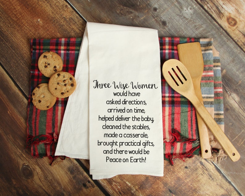 May include: White kitchen towel with black text that reads "Three Wise Women would have asked directions, arrived on time, helped deliver the baby, cleaned the stables, made a casserole, brought practical gifts, and there would be Peace on Earth!"