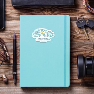 May include: A blue and white sticker with a school of fish and a yellow fish in the center. The sticker has the text "I am not afraid. I was born to do this." and the words "Be Brave" in smaller font.