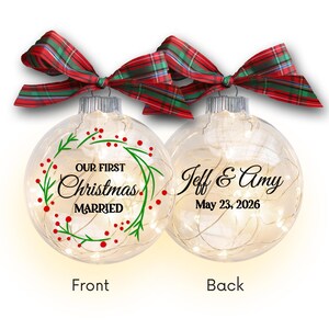 May include: Two clear Christmas ornaments with text and red and green plaid bows. One ornament says "Our First Christmas MARRIED" with a green wreath. The other says "Jeff & Amy May 23, 2026".
