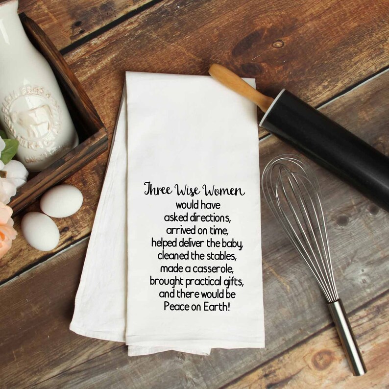 May include: White kitchen towel with black text that reads "Three Wise Women would have asked directions, arrived on time, helped deliver the baby, cleaned the stables, made a casserole, brought practical gifts, and there would be Peace on Earth!"
