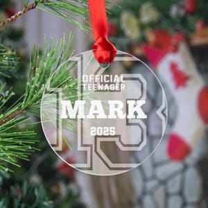 May include: Clear round Christmas ornament with the text "Official Teenager Mark 2025" in white lettering.