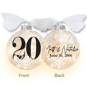May include: Clear glass Christmas ornament with the number "20" in black and the word "Years" in white. The back of the ornament has the names "Matt & Natalie" and the date "June 10, 2006". The ornament is lit with small white lights and has a white ribbon.