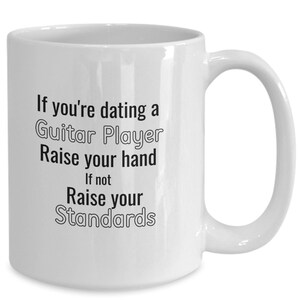 Peut inclure: Une tasse à café en céramique blanche avec du texte noir qui dit : "Si vous sortez avec un guitariste, levez la main. Sinon, relevez vos standards"