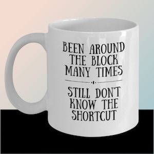 May include: White ceramic coffee mug with black text that reads "Been around the block many times... Still don't know the shortcut."