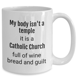 May include: White ceramic coffee mug with black text that reads "My body isn't a temple it is a Catholic Church full of wine bread and guilt"