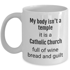 May include: White ceramic coffee mug with a black text design that reads "My body isn't a temple it is a Catholic Church full of wine bread and guilt"