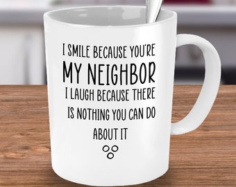 Könnte beinhalten: Weiße Keramik-Kaffeetasse mit schwarzem Text, der lautet: "Ich lächle, weil du mein Nachbar bist. Ich lache, weil du nichts dagegen tun kannst." Die Tasse hat zwei kleine Kreise am Boden.