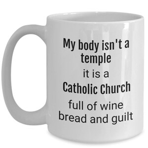 May include: White ceramic coffee mug with black text that reads "My body isn't a temple it is a Catholic Church full of wine bread and guilt"
