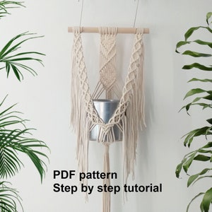 May include: A white macrame plant hanger with a metal pot hanging from it. The hanger is made with a knot pattern and has long fringe. The text "PDF pattern Step by step tutorial" is written below the hanger.
