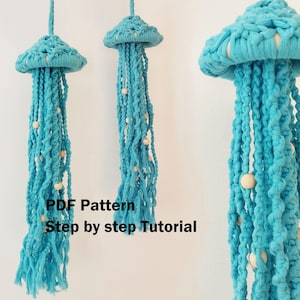 Puede incluir: Tres decoraciones colgantes de medusas de macramé en tonos turquesa. Cada medusa presenta una parte superior redondeada con hebras largas y fluidas y cuentas de madera. El texto "PDF Pattern Step by step Tutorial" es visible.