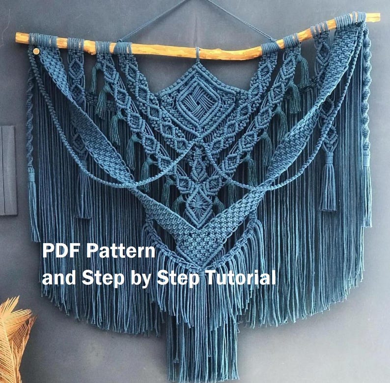 Op de afbeelding: Een blauwe macram&eacute; wandhanger met een geometrisch ontwerp en franjes. De hanger is bevestigd aan een houten tak. De tekst "PDF Pattern and Step by Step Tutorial" is onder de hanger gedrukt.
