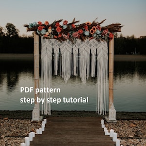 May include: A white macrame wedding arch decorated with flowers and greenery, set up outdoors on a wooden walkway with candles lining the path. The arch is made of natural materials and has a rustic, bohemian feel. The text "PDF pattern step by step tutorial" is visible at the bottom of the image.