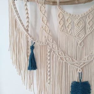 May include: A macrame wall hanging with a natural wood dowel and a white cotton cord. The hanging features a variety of knot patterns and has teal blue tassels.