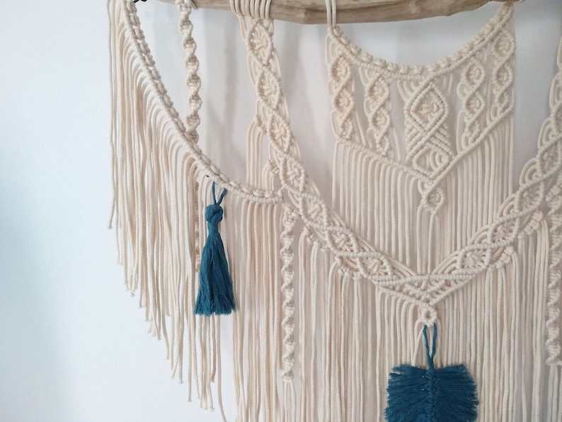 May include: A macrame wall hanging with a natural wood dowel and a white cotton cord. The hanging features a variety of knot patterns and has teal blue tassels.