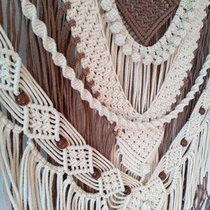 May include: A white and brown macrame wall hanging with wooden beads. The macrame is made with a variety of knots and patterns, and the beads are spaced evenly throughout the hanging.