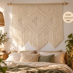 May include: A large off-white macrame wall hanging featuring three prominent diamond-shaped patterns and long fringe, suspended from a wooden rod. A circular badge on the right side contains the text PDF tutorial with a small leaf graphic.