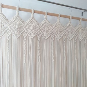 May include: A white macrame wall hanging with a geometric pattern. The hanging is made of cotton cord and is attached to a wooden dowel rod.